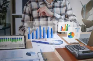 Imagem de um homem com camisa xadrez, sentando de frente para uma mesa, analisando gráficos e dados