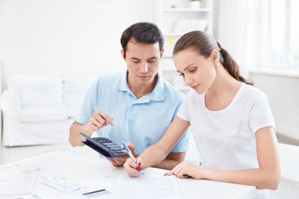 Imagem de um homem e uma mulher sentados em frente a uma mesa com vários papéis, caneta e calculadora